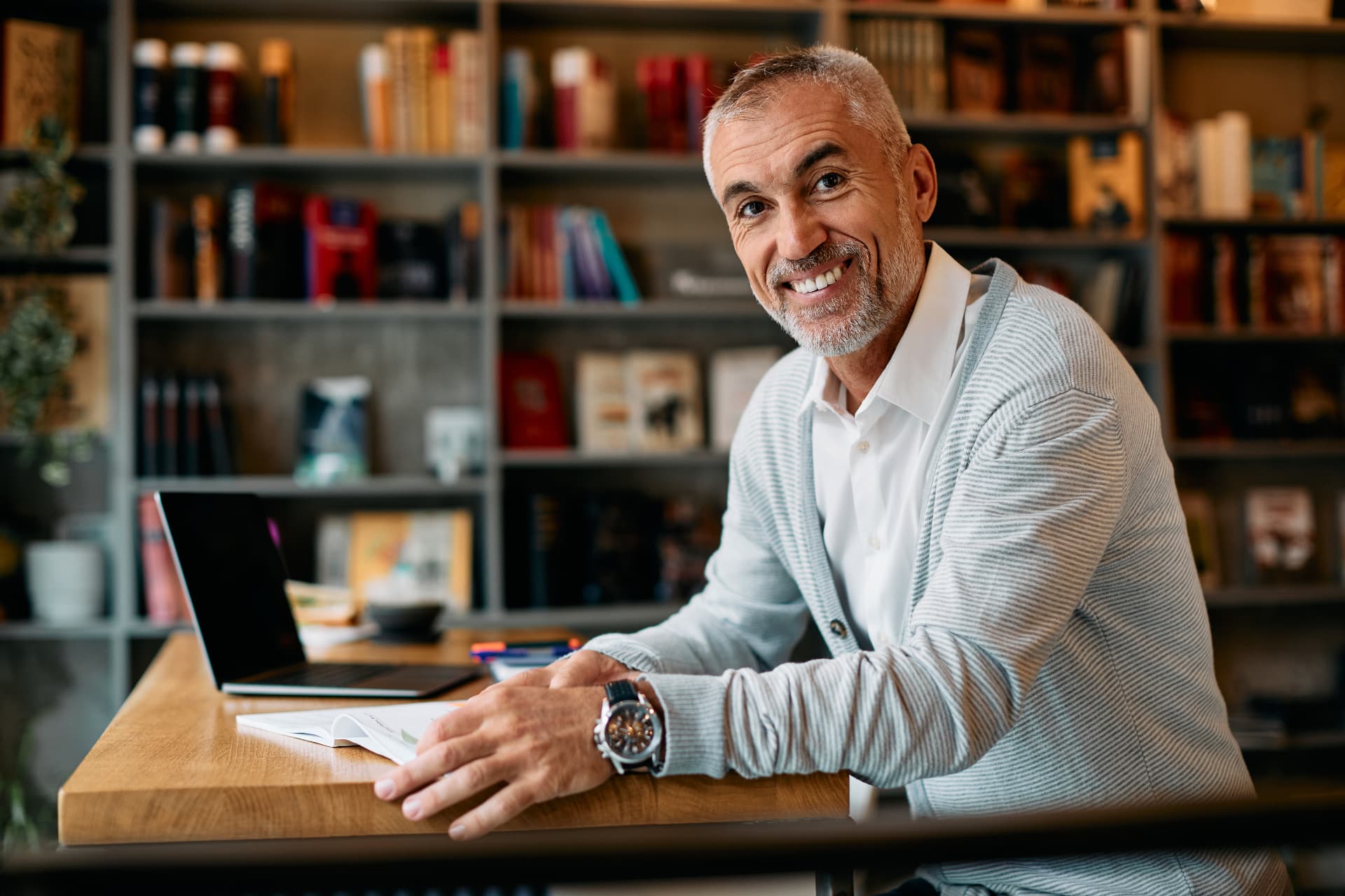 Business owner smiling at his desk in a library-lined study