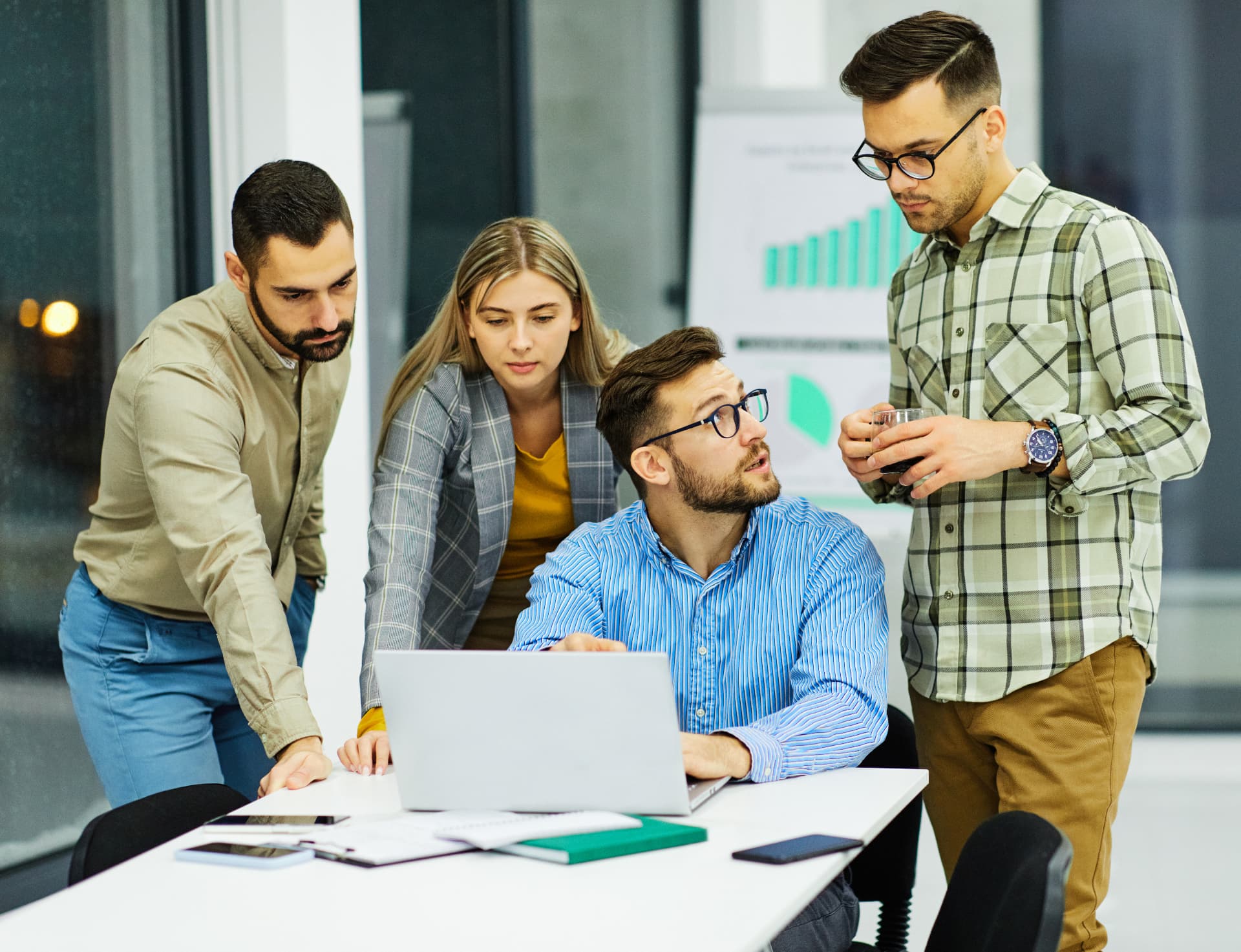 Four colleagues gathered around a laptop in a modern office, one pointing at the screen