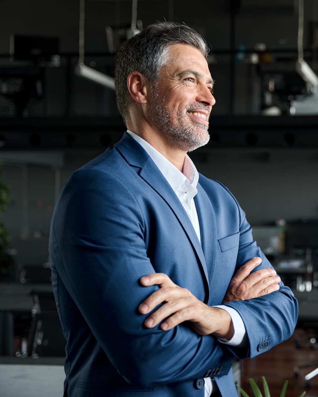 Businessman in a blue suit smiling with arms crossed in a modern office